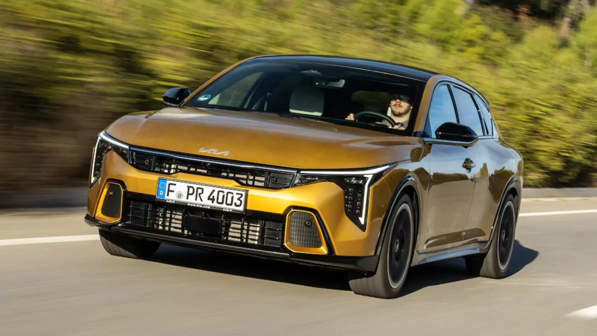 Kia K4 berline compacte thermique vue de trois-quarts avant sur route, design sportif avec toit flottant